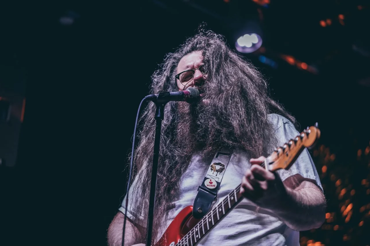 Kelsey Hudgins singing and playing his red electric guitar on stage